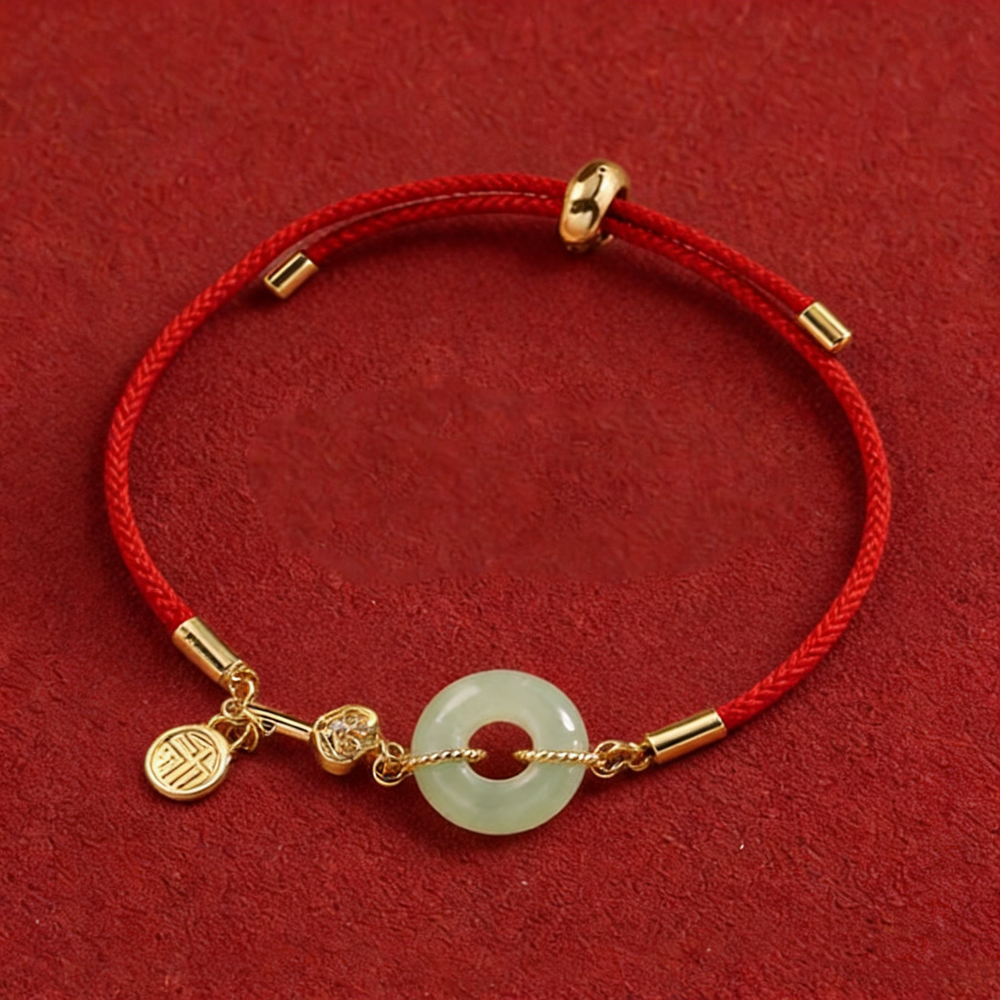 Bracelet with red cord, gold accents, and a jade charm on a red background