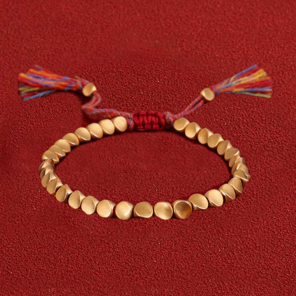 Gold beaded bracelet with colorful tassels on a red background