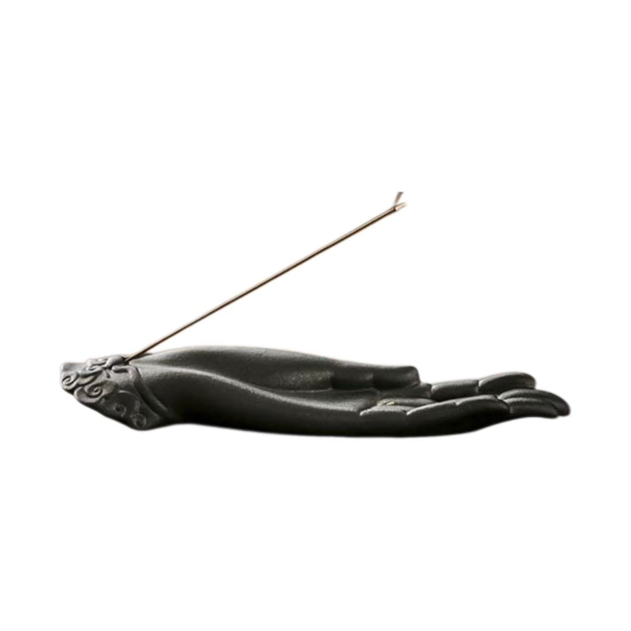 Incense stick in a hand-shaped holder with a teapot and cups on a wooden table