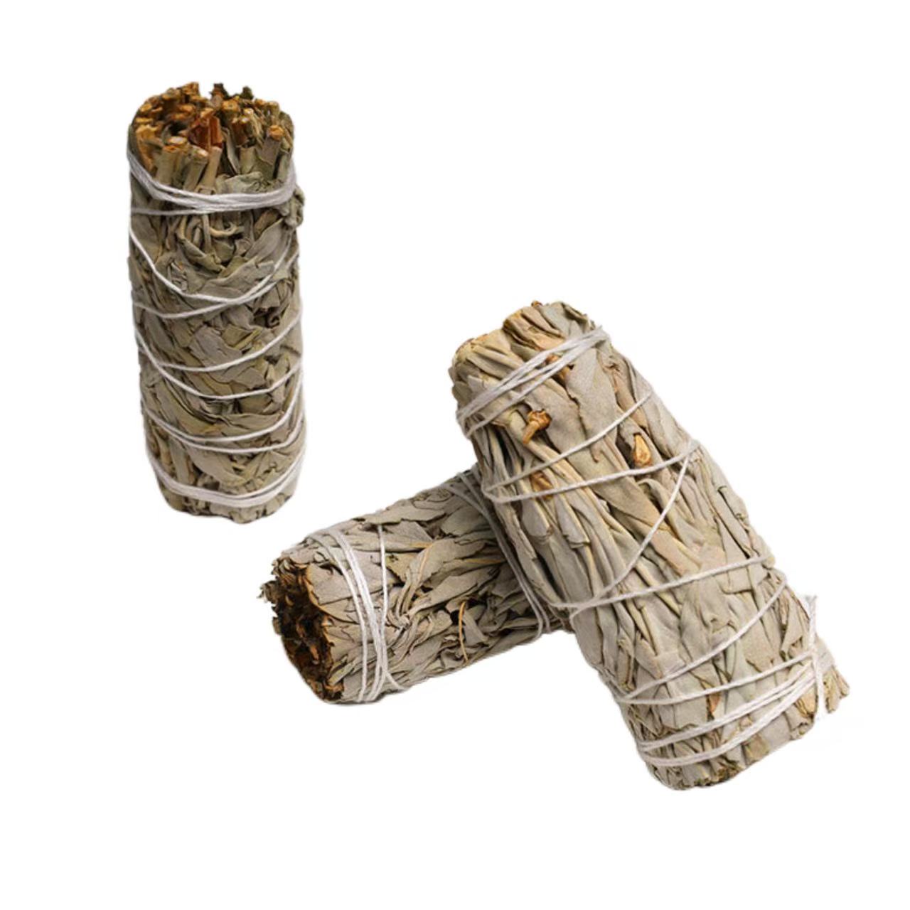 Two bundles of sage wrapped in twine on a wooden surface with a crystal.