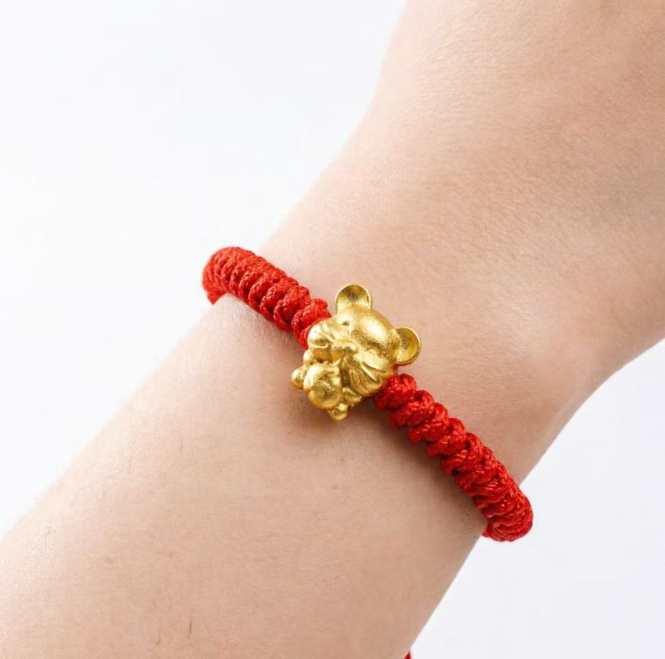Red string bracelet with a gold charm on a wrist against a white background