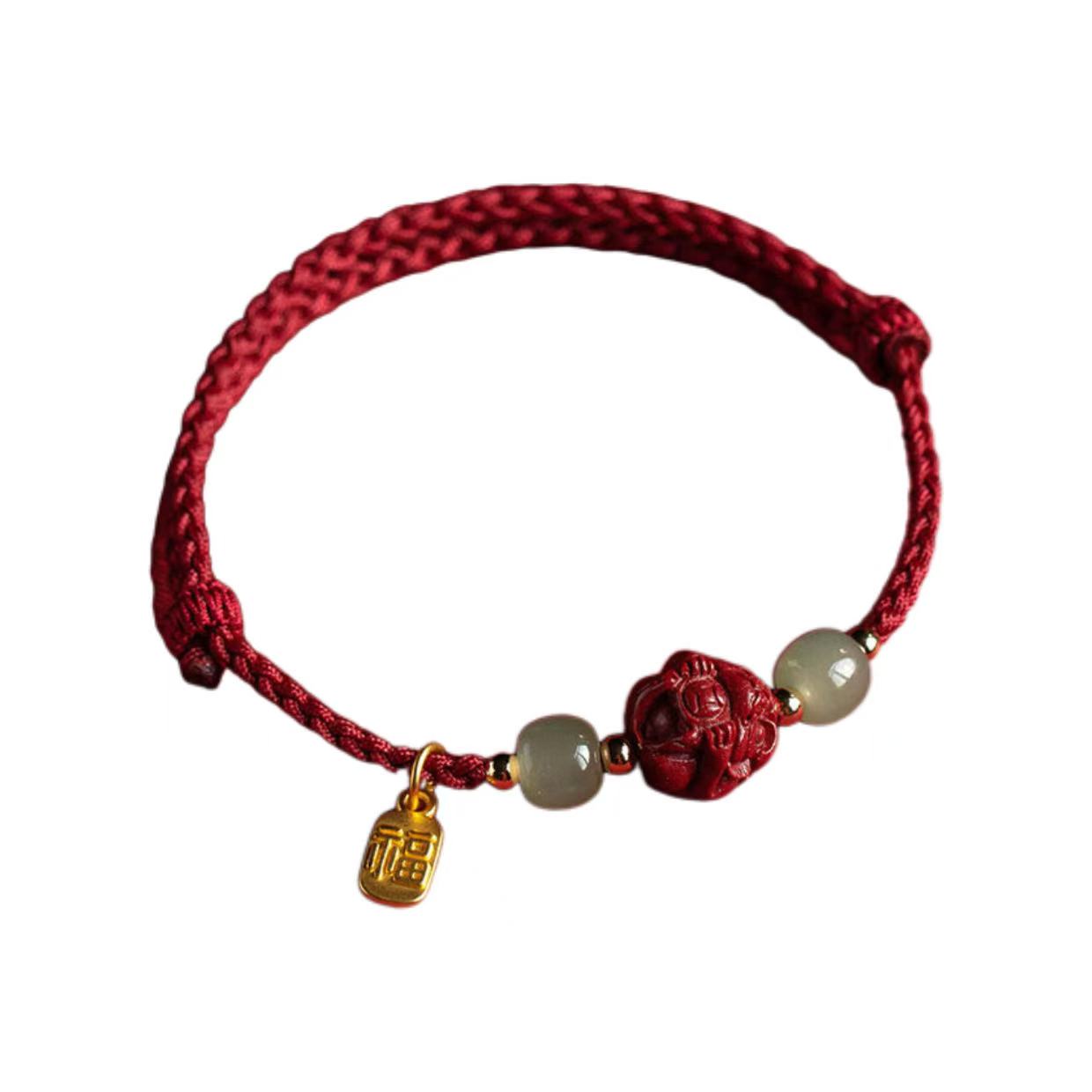 Red braided bracelet with gold charm and red ball on a white background