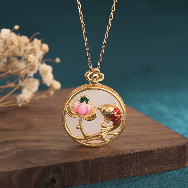 Gold necklace with a round pendant featuring a fish and lotus flower on a wooden surface.
