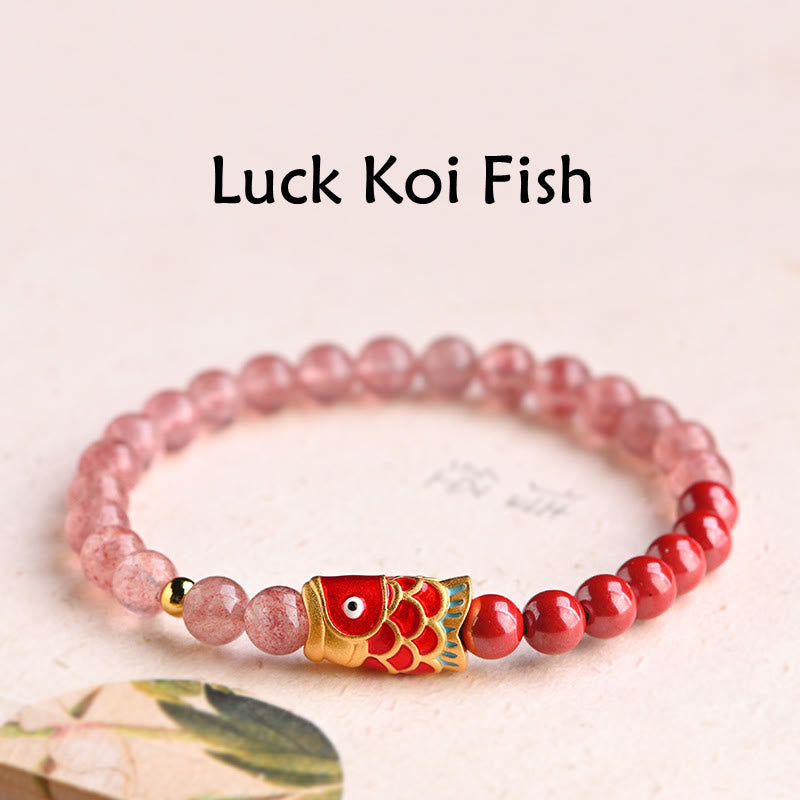 Bracelet with red and pink beads and a gold fish charm on a light pink background.