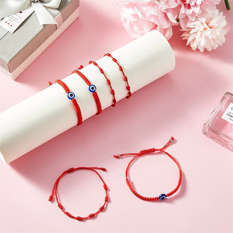 Red string bracelets with blue beads on a pink surface with flowers and a gift box.