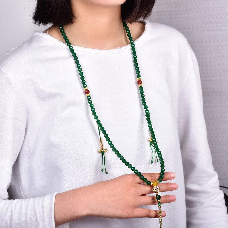 Person wearing a long green beaded necklace with a white shirt.