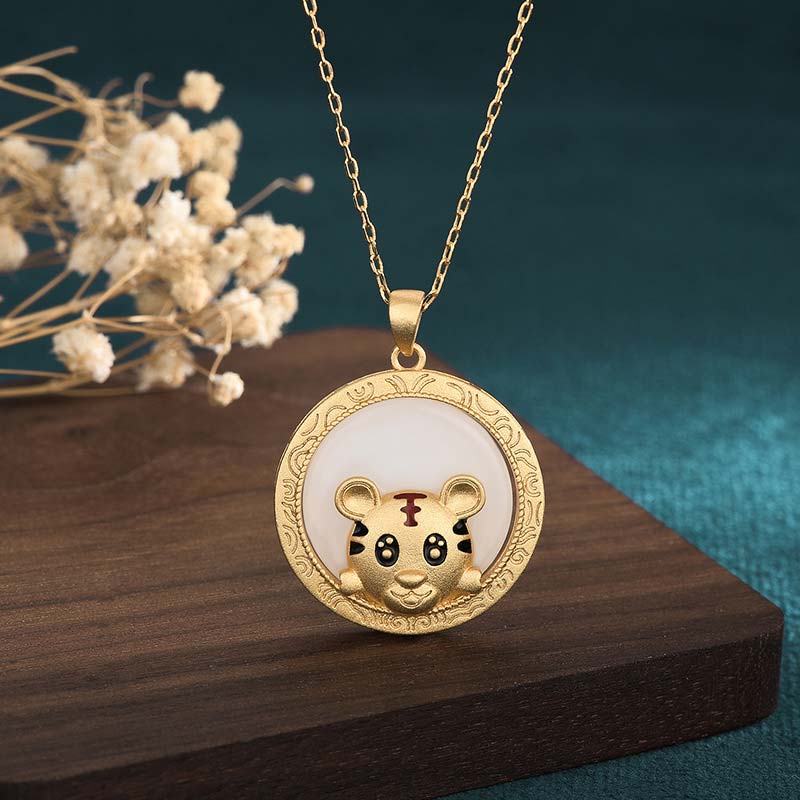 Gold necklace with a tiger pendant on a wooden surface with dried flowers.