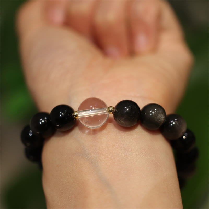 Black beaded bracelet with a clear central bead on a wrist against a blurred background