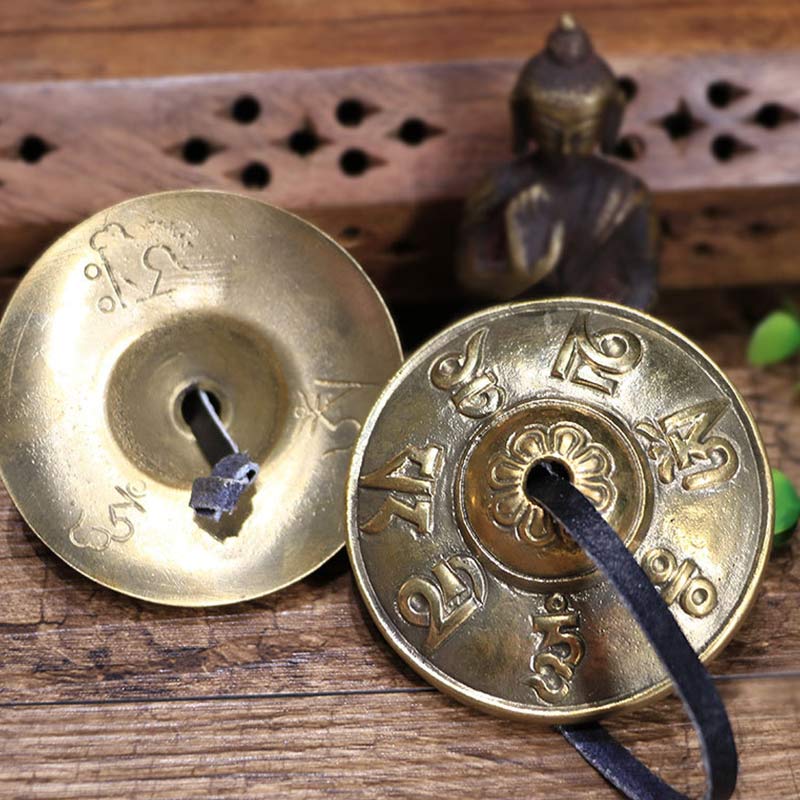 Two brass cymbals with intricate designs on a wooden surface.