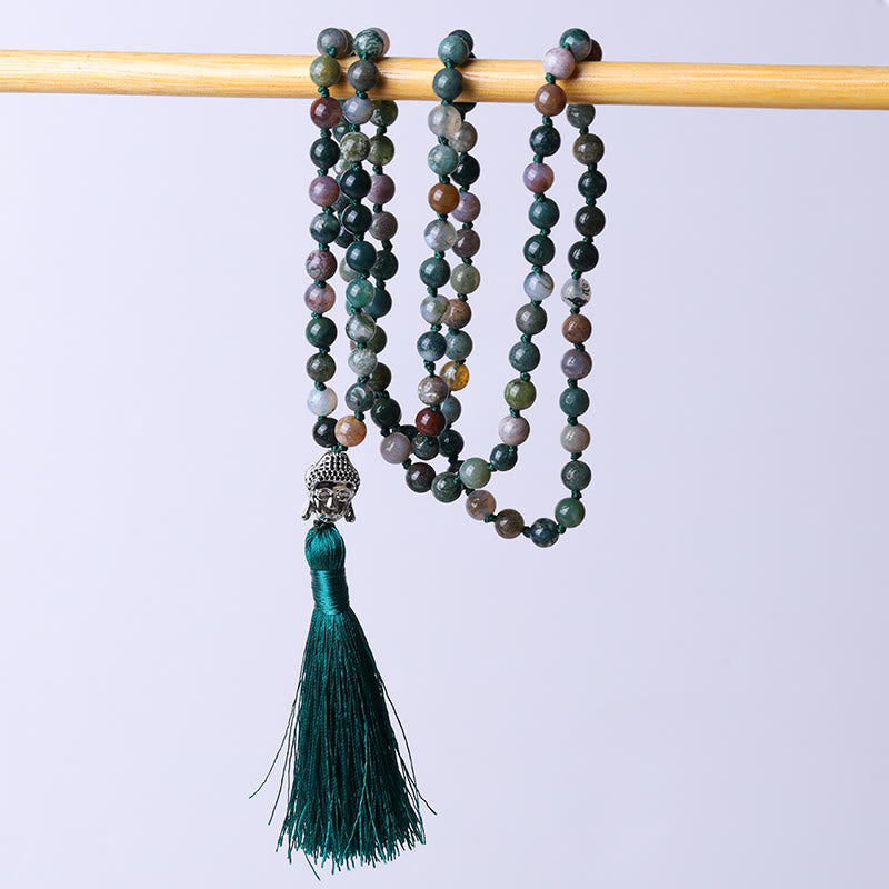 Beaded necklace with a tassel on a wooden stick against a light purple background