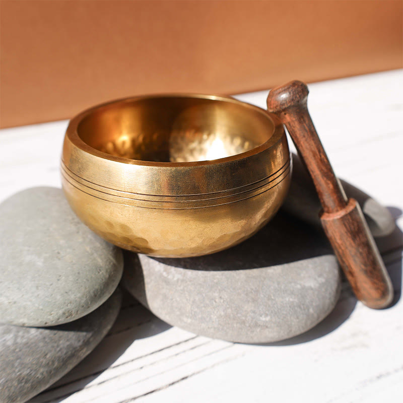 Gold singing bowl with wooden striker on gray stones
