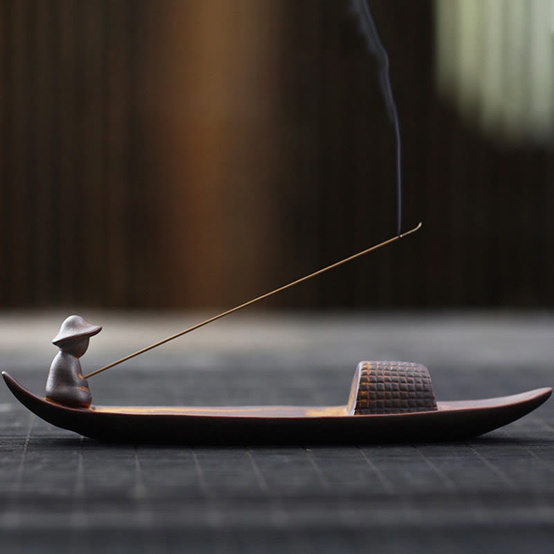 Incense burner with a small figure on a boat and incense stick on a dark surface