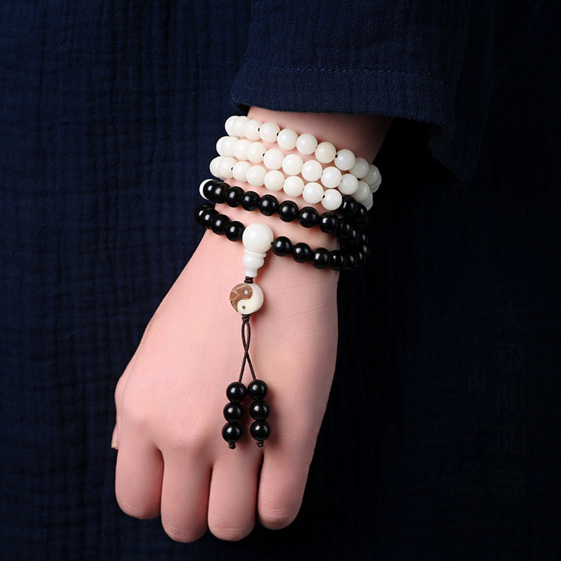 Hand wearing multiple black and white beaded bracelets on a dark background