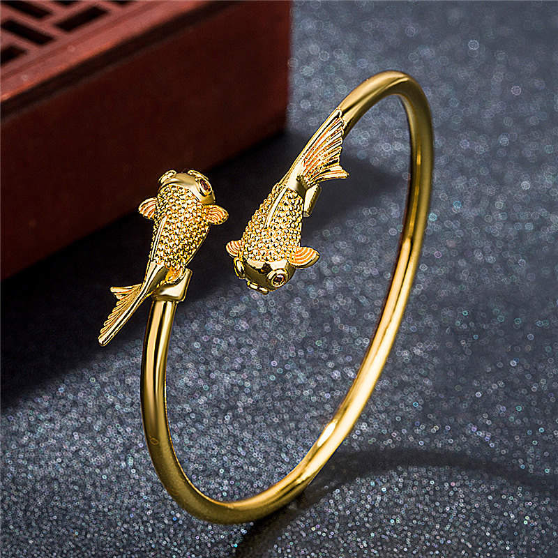 Gold bracelet with fish designs on a dark textured surface