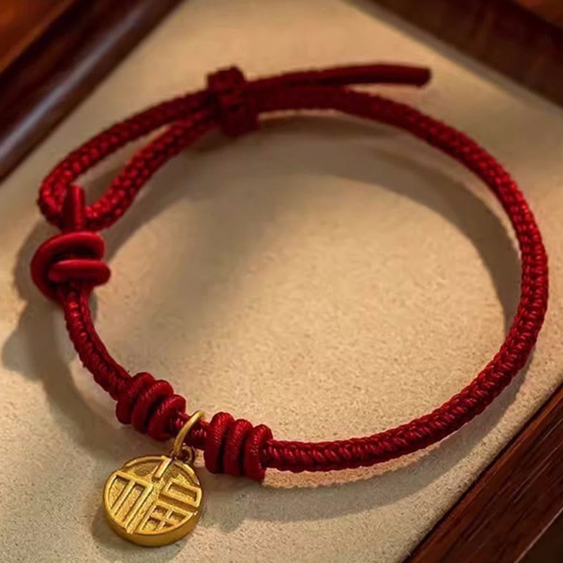 Red string bracelet with a gold charm on a textured surface