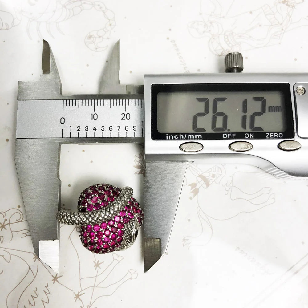 Ring with pink gemstones being measured by a digital caliper on a white background.