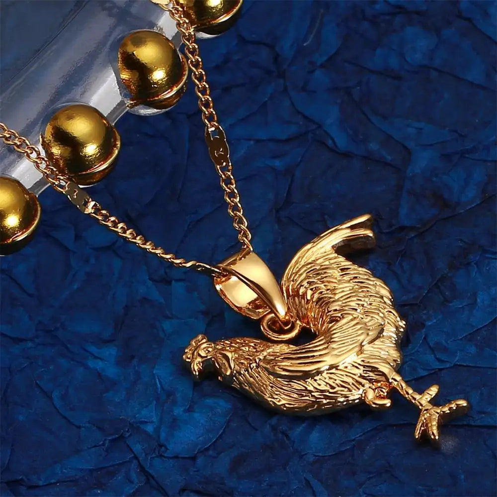 Gold rooster pendant on a chain against a blue textured background
