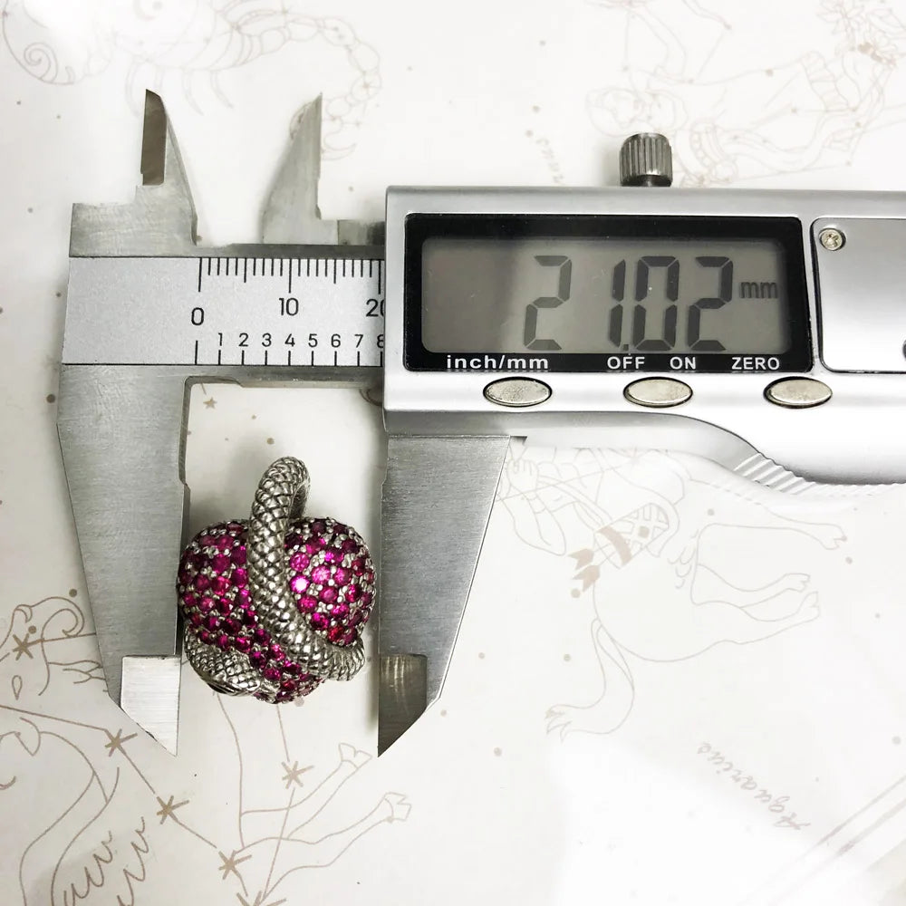 Digital caliper measuring a decorative brooch with pink gemstones on a white background.