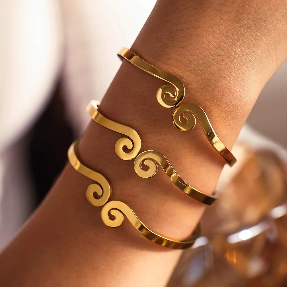 Gold bracelet with intricate designs on a wrist against a neutral background