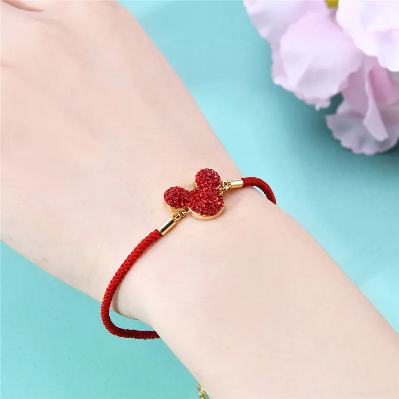 Red bracelet with a gold Mickey Mouse head charm on a wrist against a light blue background