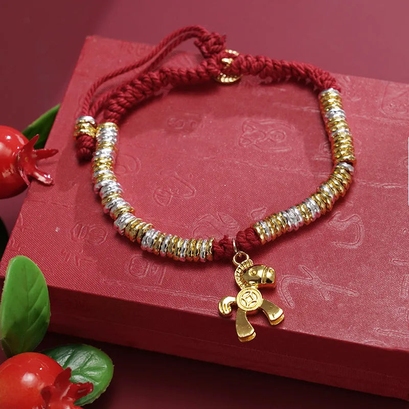 Bracelet with gold and silver beads and a teddy bear charm on a red textured surface.