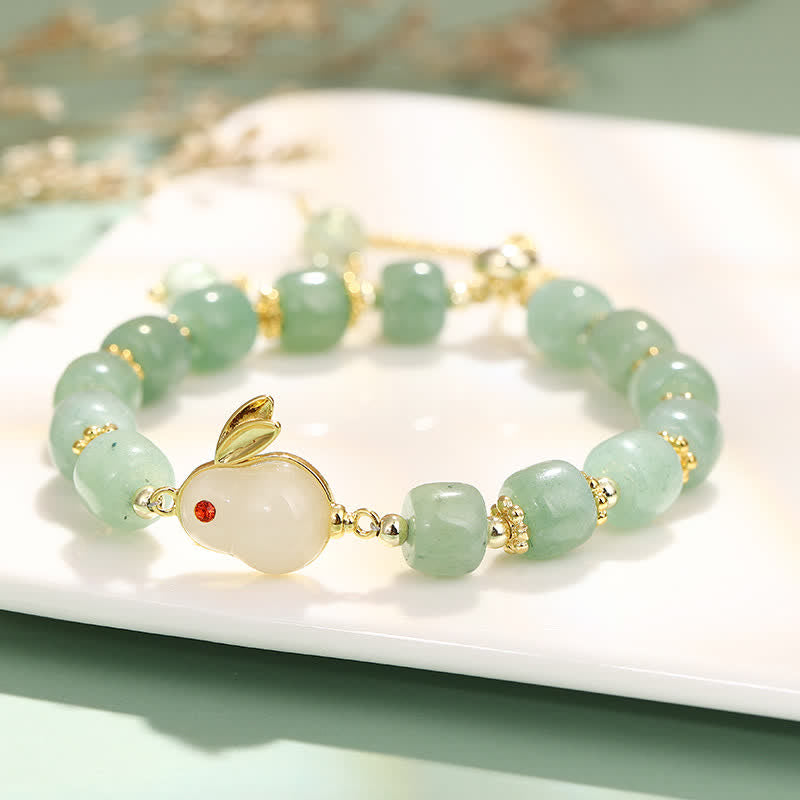 Green beaded bracelet with a gold bunny charm on a white surface