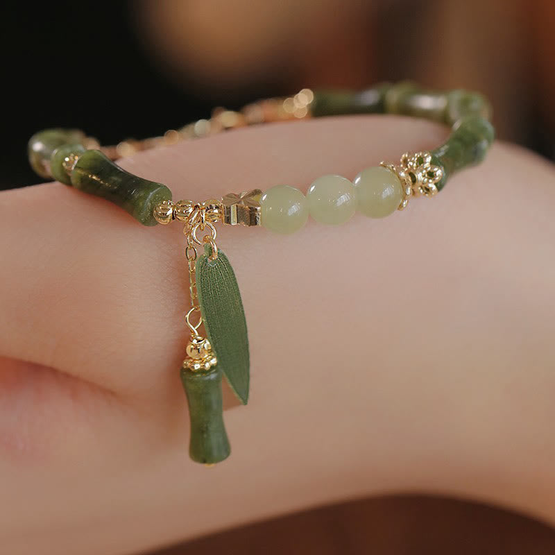 Green beaded bracelet with gold accents and a leaf charm on a wrist.