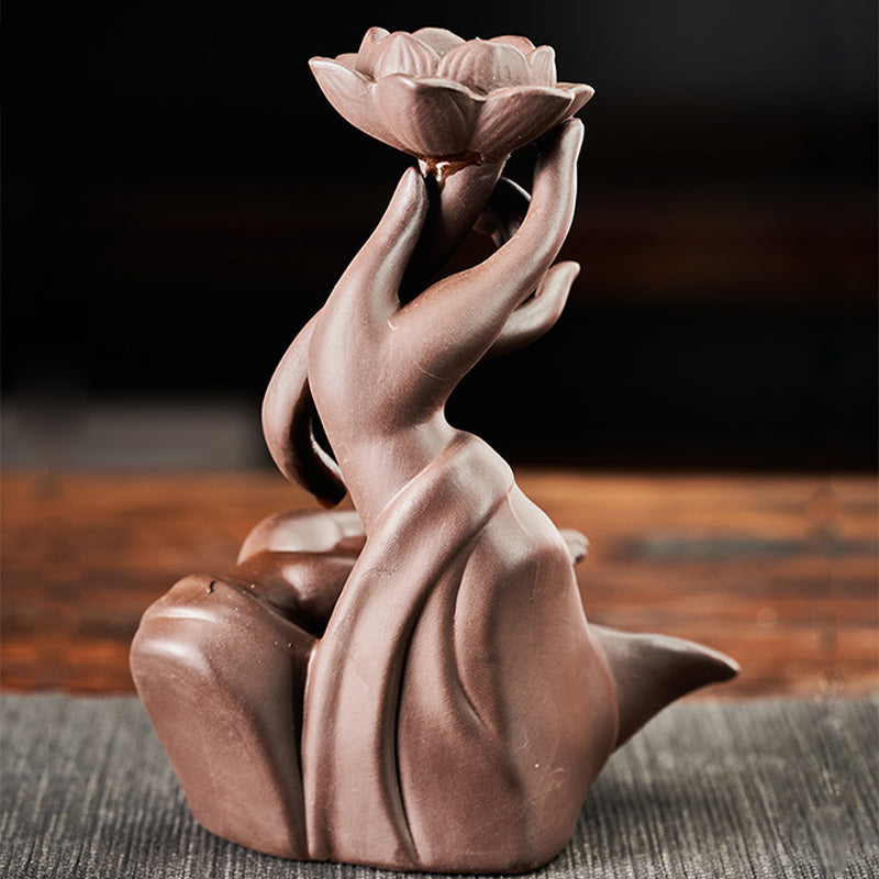 Ceramic sculpture of a hand holding a lotus flower on a wooden surface.