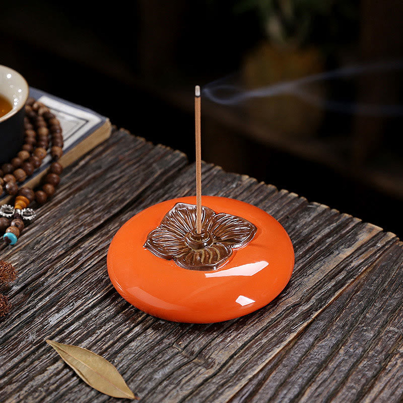 Incense burner with a smoking incense stick on an orange base, placed on a wooden surface.