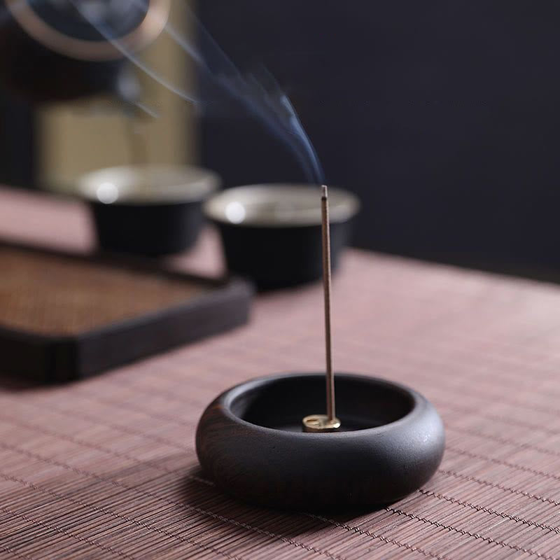 Incense stick burning in a black holder on a textured surface with a blurred background