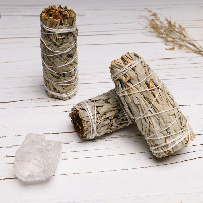 Two bundles of sage wrapped in twine on a wooden surface with a crystal.