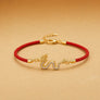 Gold bracelet with a red cord and dragon charm on a beige background