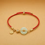 Bracelet with gold accents and a red cord on a beige background