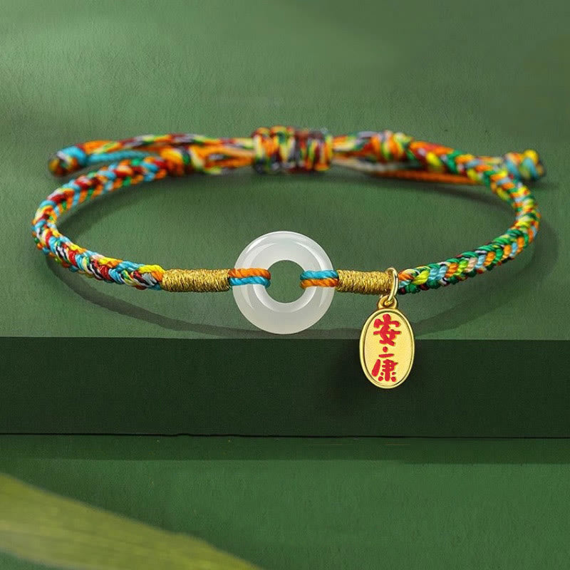 Colorful braided bracelet with a gold charm and a circular pendant on a green background