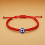 Red bracelet with a blue evil eye charm on a beige background