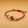 Red string bracelet with gold and pearl charms on a beige background