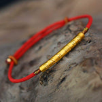 Close-up of gilded silver Tibetan mantra bracelet handmade with red cord
