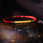 Gilded silver Tibetan mantra bracelet displayed on traditional setting with warm light