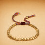 Gold beaded bracelet with colorful cord on a beige background